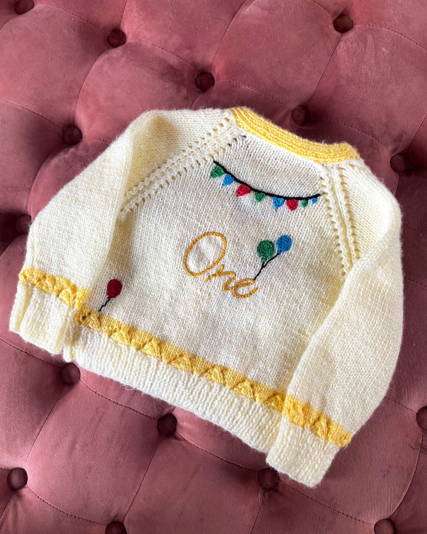 Hand knitted white and yellow baby cardigan with balloons and bunting design, unique first birthday cardigan gift