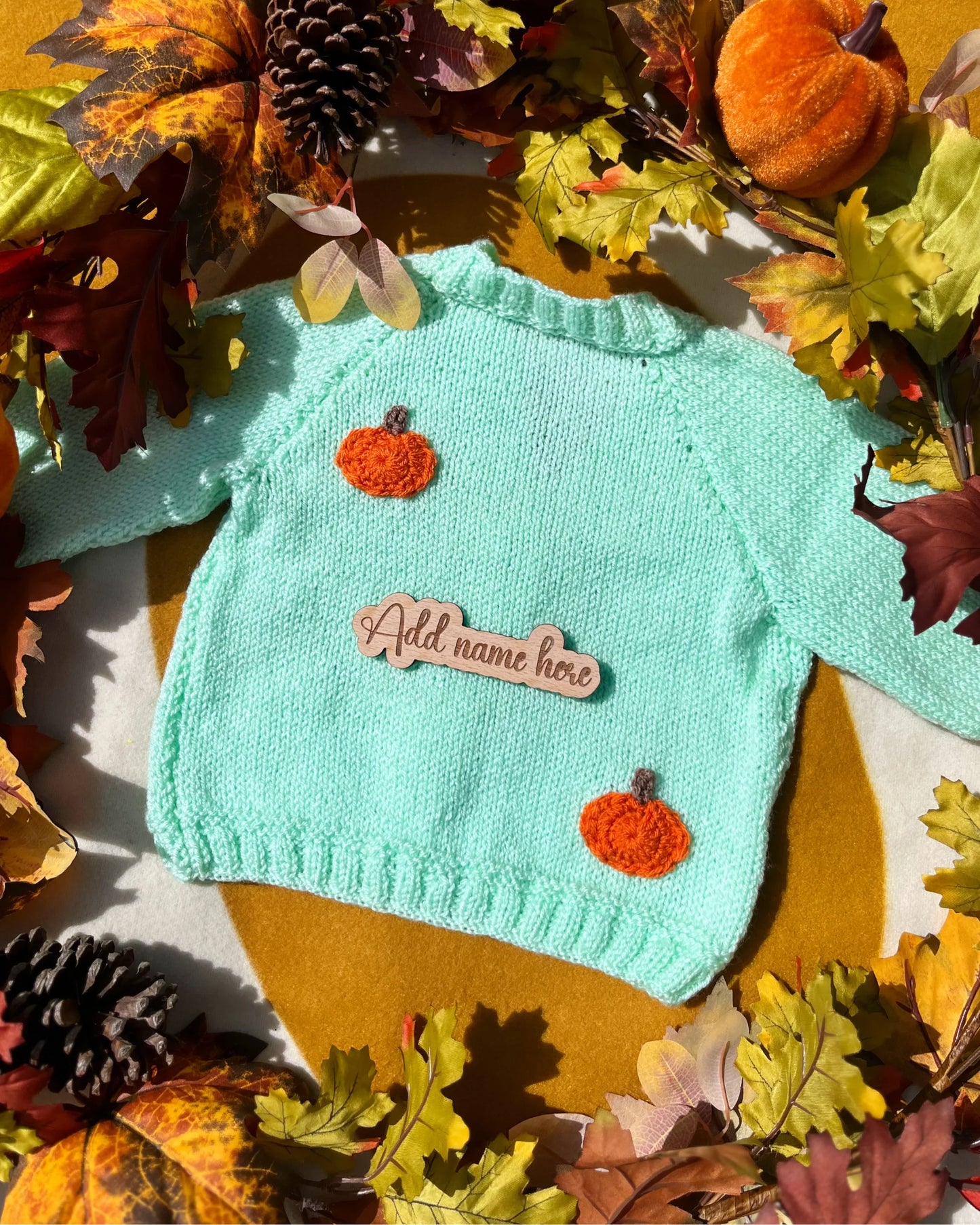 Mint green handknit toddler sweater with orange pumpkin appliques and wooden name tag in autumn custom pumpkin outfit for toddlers