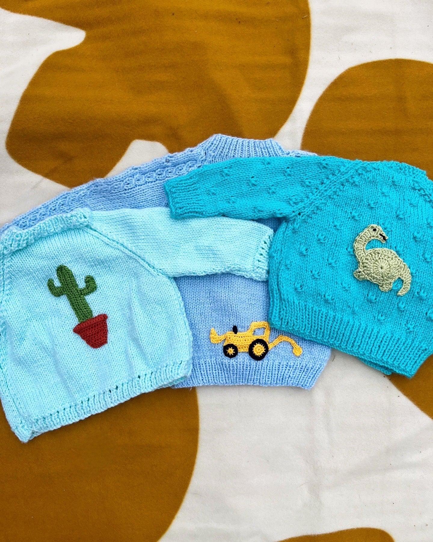 Three handmade personalised baby boy cardigans in pastel blue shades with knitted cactus, digger, and crab buttons