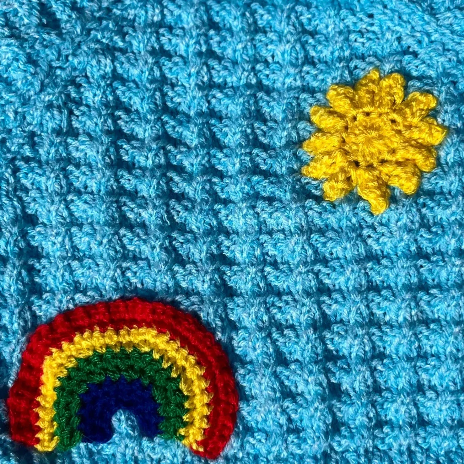 Blue crocheted blanket with rainbow and yellow flower appliques from Little Flower Knits personalised newborn baby knitwear