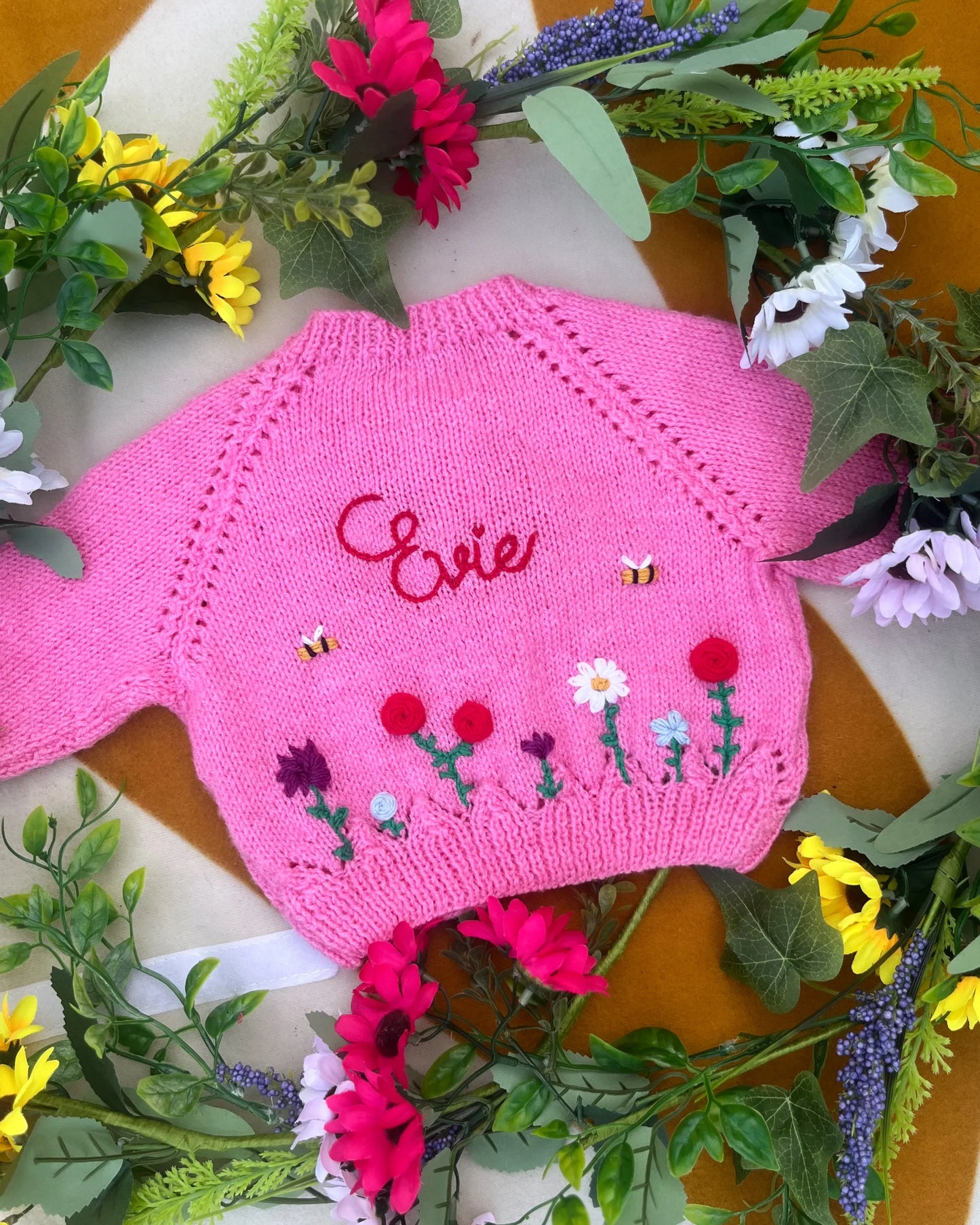 Pink personalised baby cardigan UK with floral embroidery and name Evie by Little Flower Knits surrounded by colourful flowers