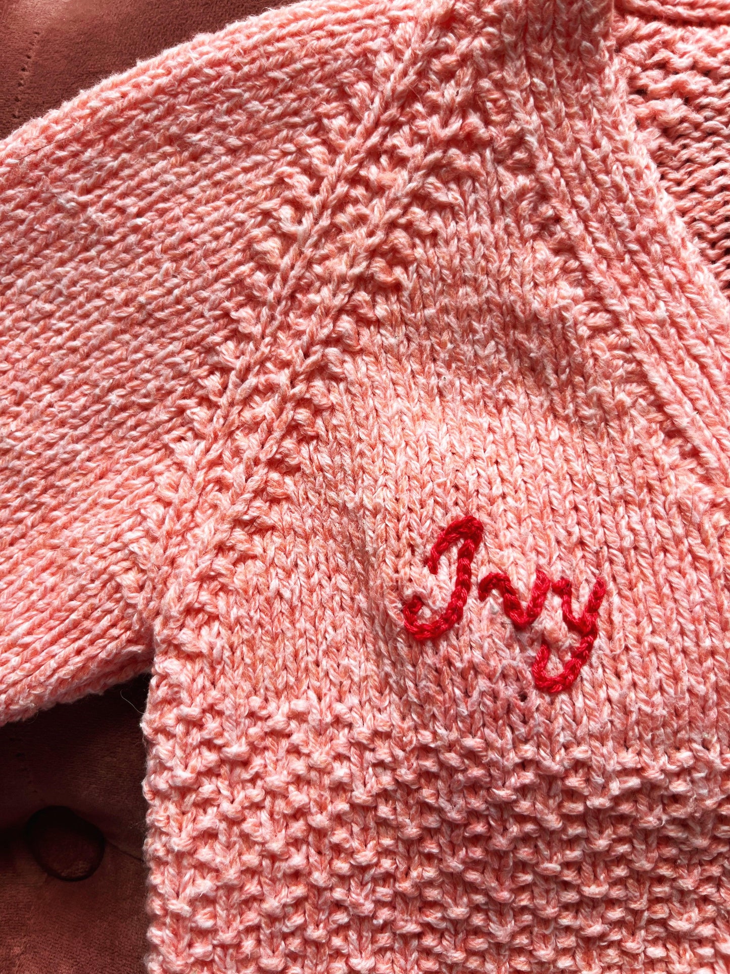 Close-up of a pink knitted personalised baby cardigan UK with the name Ivy embroidered in red