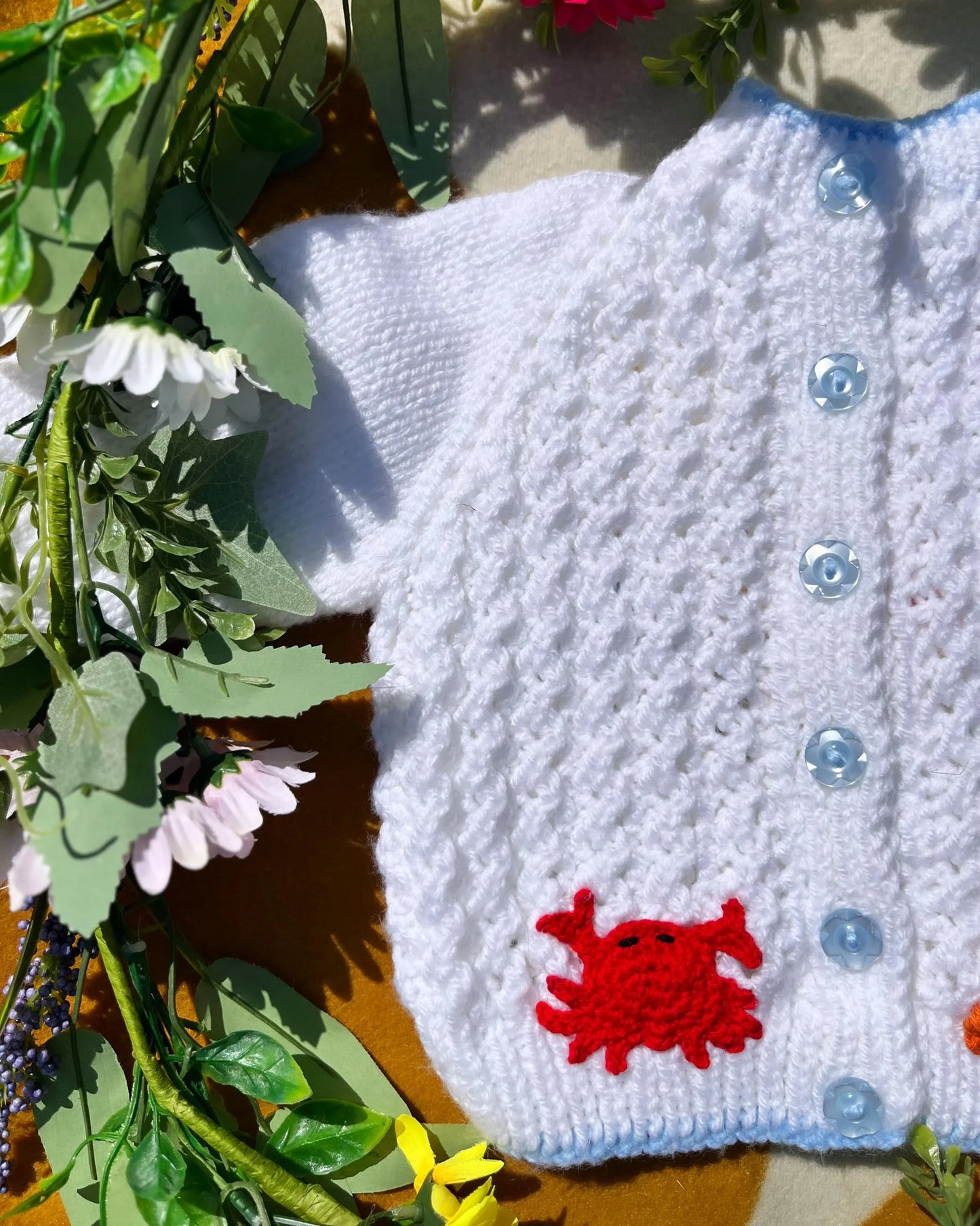 Hand-knitted white personalised mermaid cardigan with blue buttons and red crab detail by Little Flower Knits