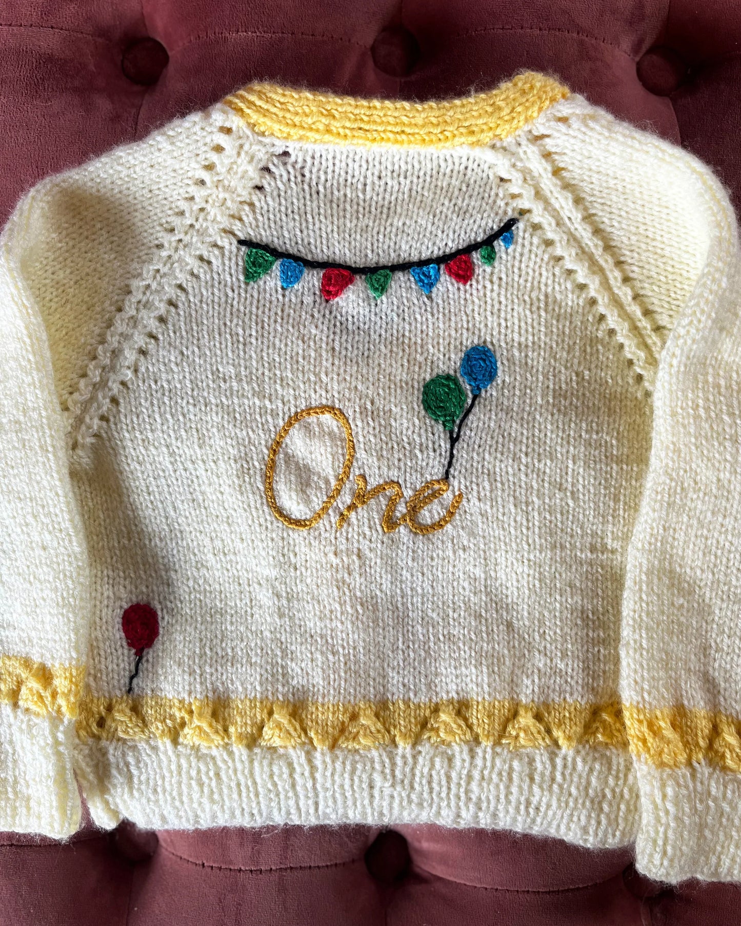 Handknitted baby cardigan with yellow trim and embroidered balloons and banner, unique first birthday cardigan gift