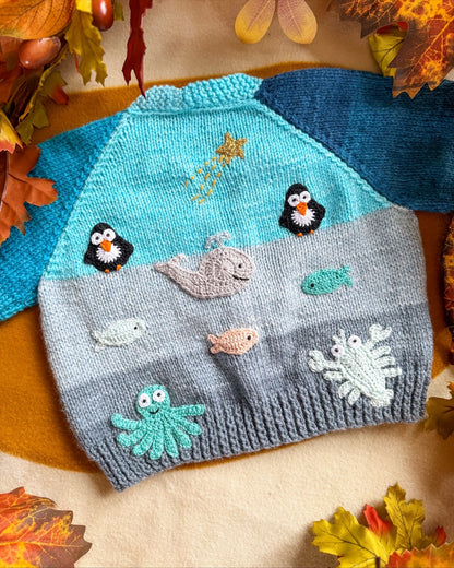 Arctic animals baby cardigan featuring colourful penguins, whales, and sea creatures on a soft knit background