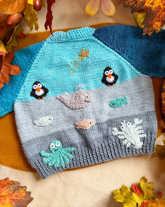 Arctic animals baby cardigan featuring colourful penguins, whales, and sea creatures on a soft knit background
