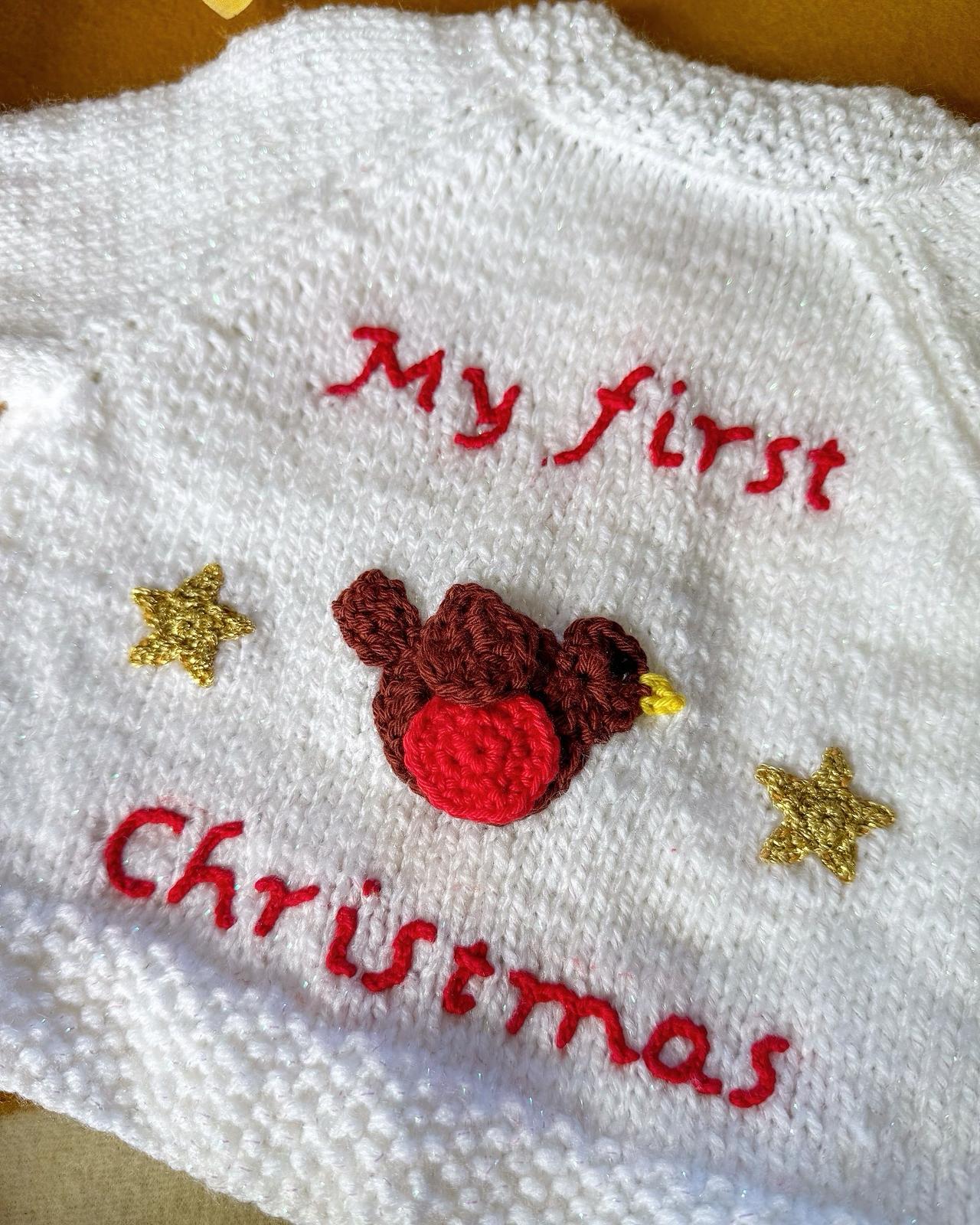 White baby's first Christmas cardigan with red text and a cute bird design on the back