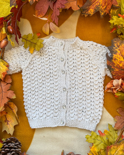Hand-knitted baby cardigan in soft cream, perfect for layering with a Christmas tree cardigan baby theme