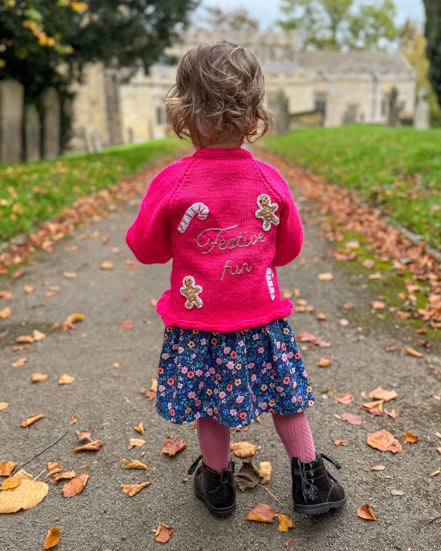 Cute girl in a pink festive personalised kids cardigan with candy and gingerbread decor outdoors