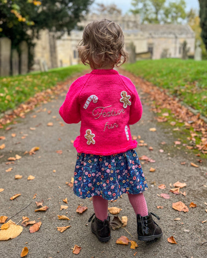 Cute girl in a pink festive personalised kids cardigan with candy and gingerbread decor outdoors