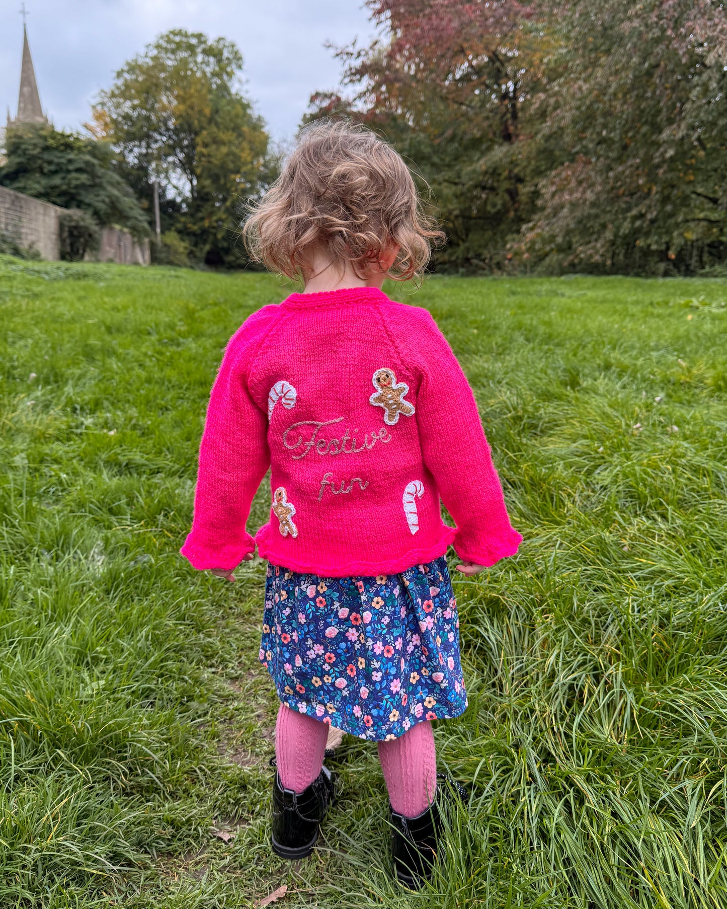 Bright pink festive personalised kids cardigan featuring candy cane and gingerbread embellishments