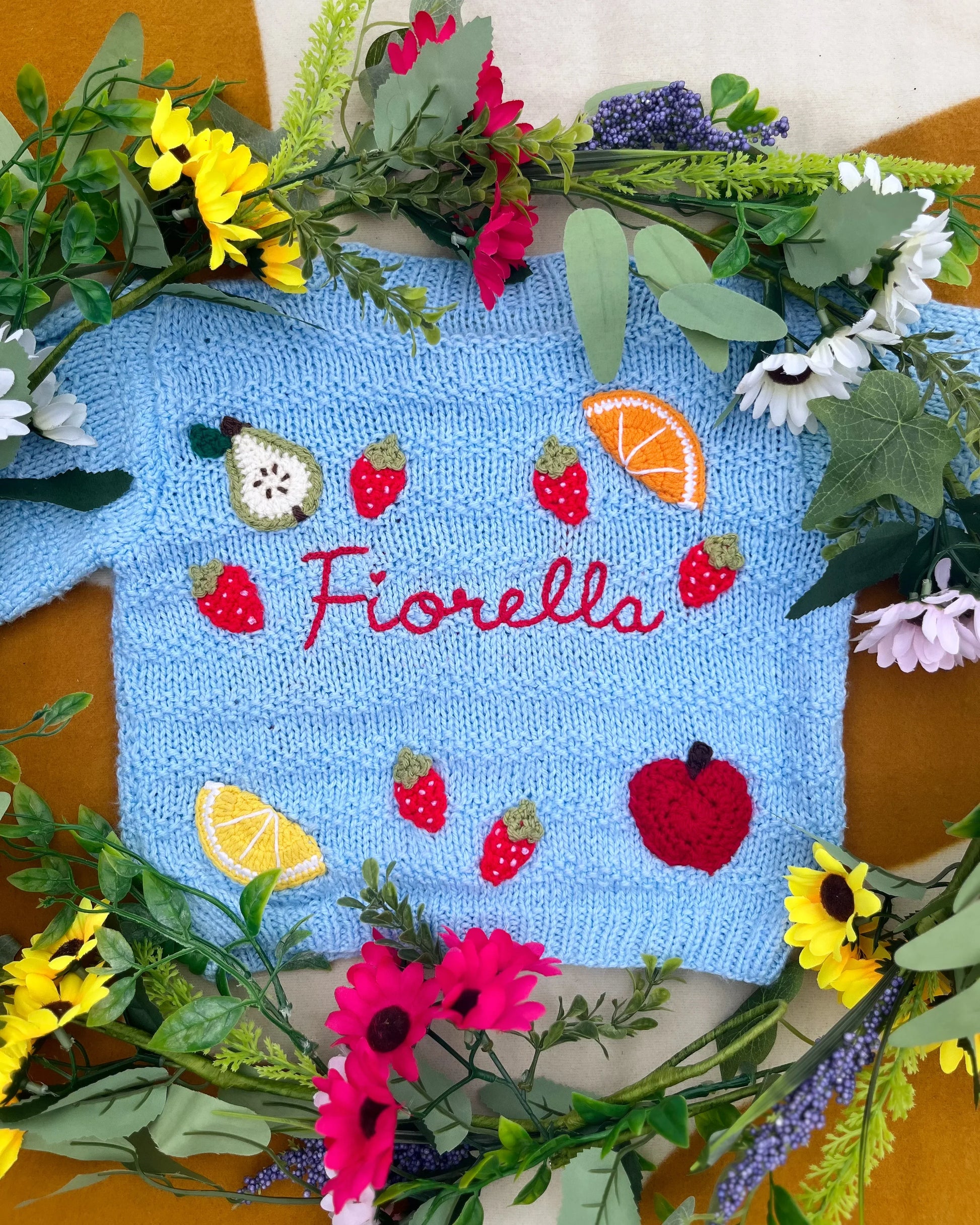 Little Flower Knits fruit pattern cardigan for toddlers in blue with colourful fruit designs and embroidered name Fiorella