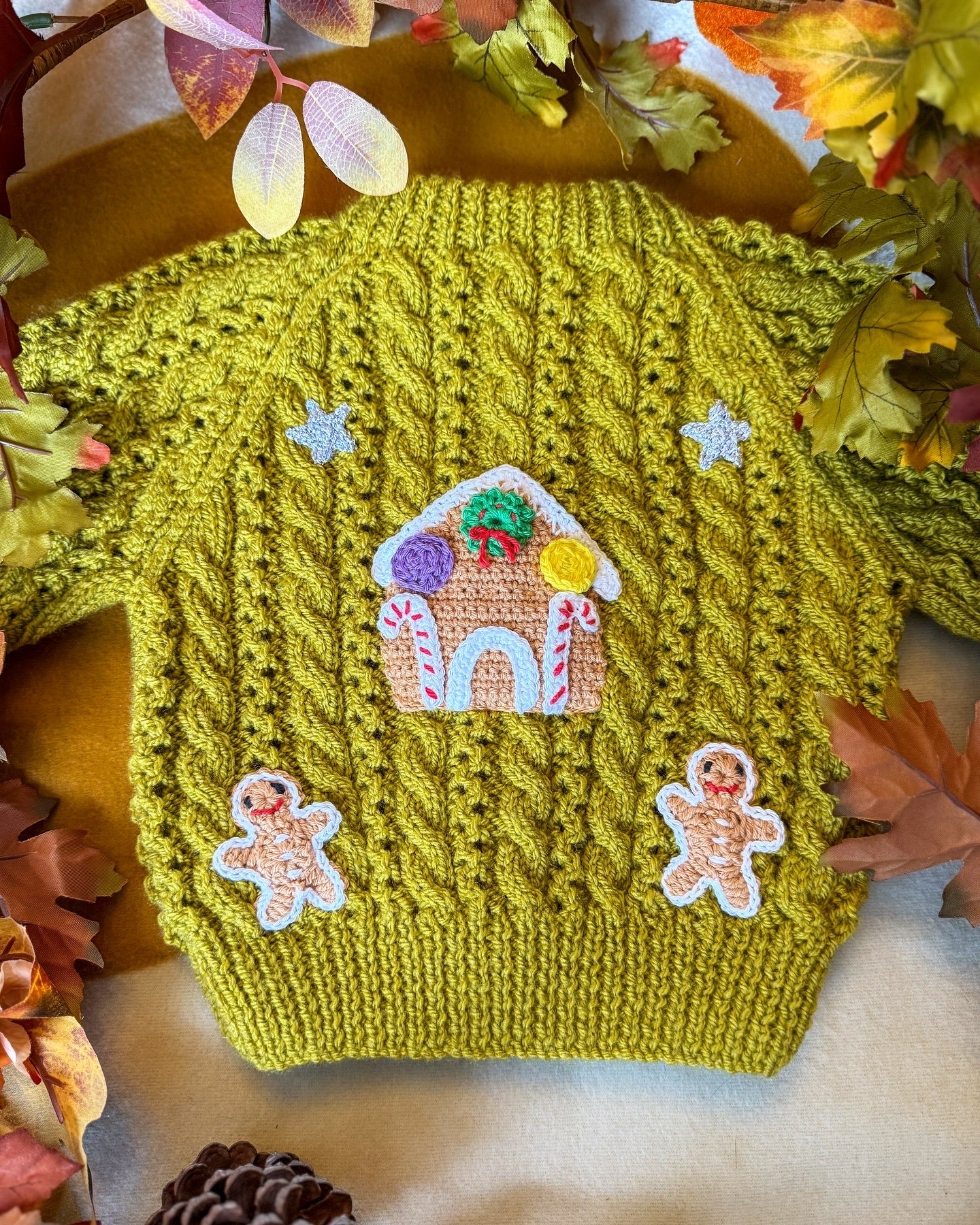 Gingerbread cottage baby cardigan in green with whimsical holiday embroidery and a textured cable knit design