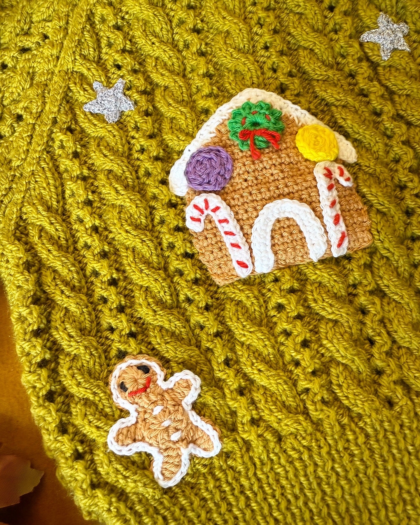 Close-up of gingerbread cottage baby cardigan featuring festive gingerbread house and star accents