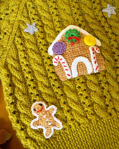 Close-up of gingerbread cottage baby cardigan featuring festive gingerbread house and star accents