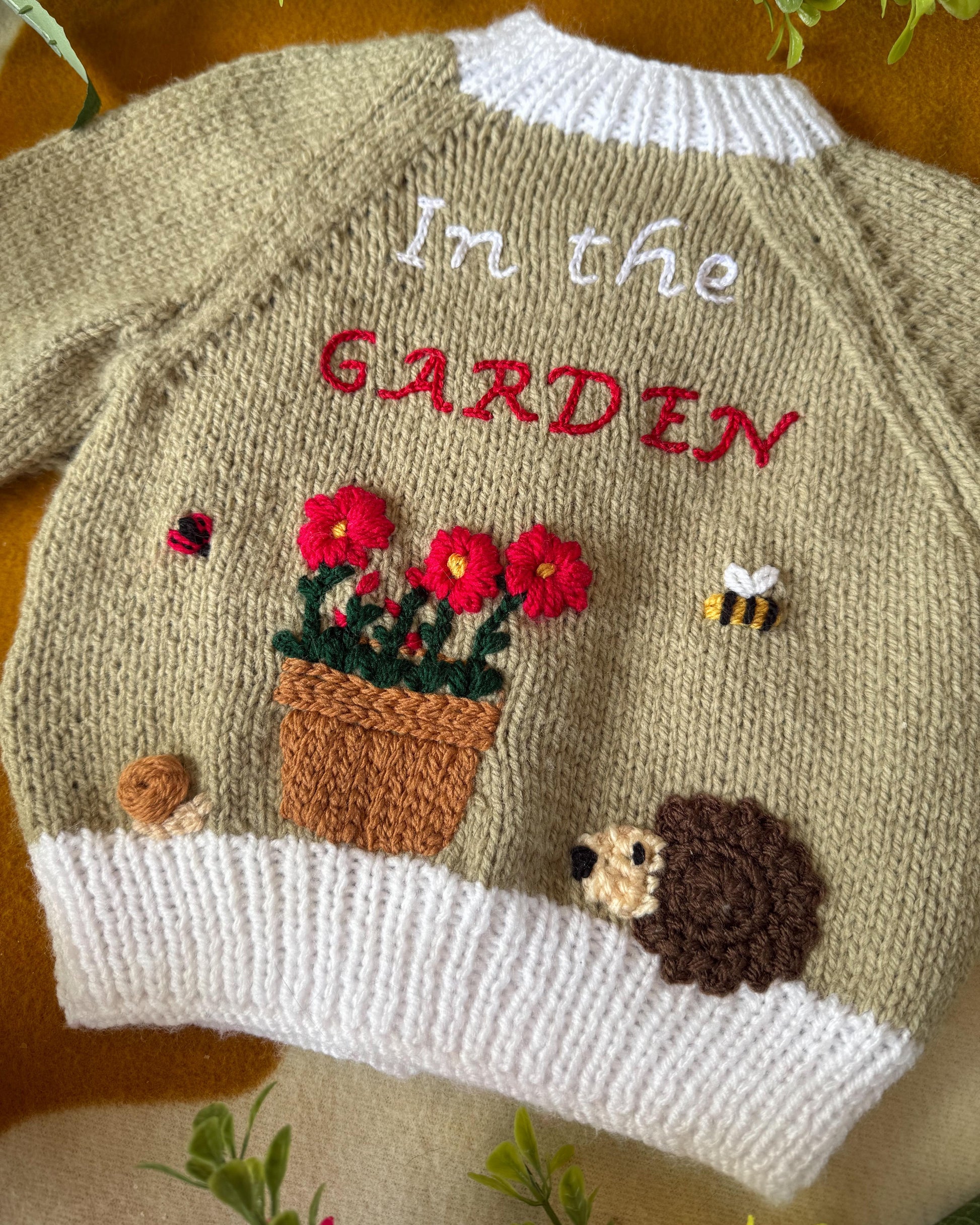 Handmade baby cardigan UK featuring hedgehog and garden theme with floral embroidery
