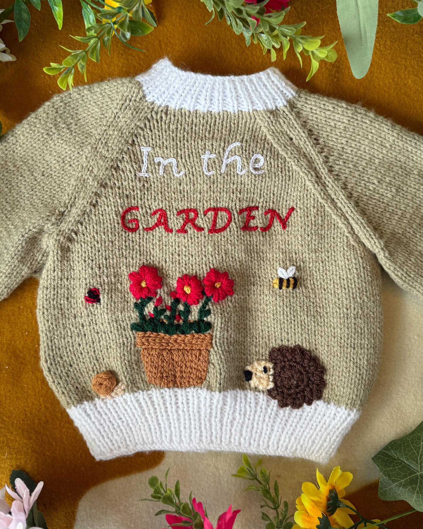 Handmade baby cardigan UK featuring floral garden embroidery and hedgehog detail from Little Flower Knits
