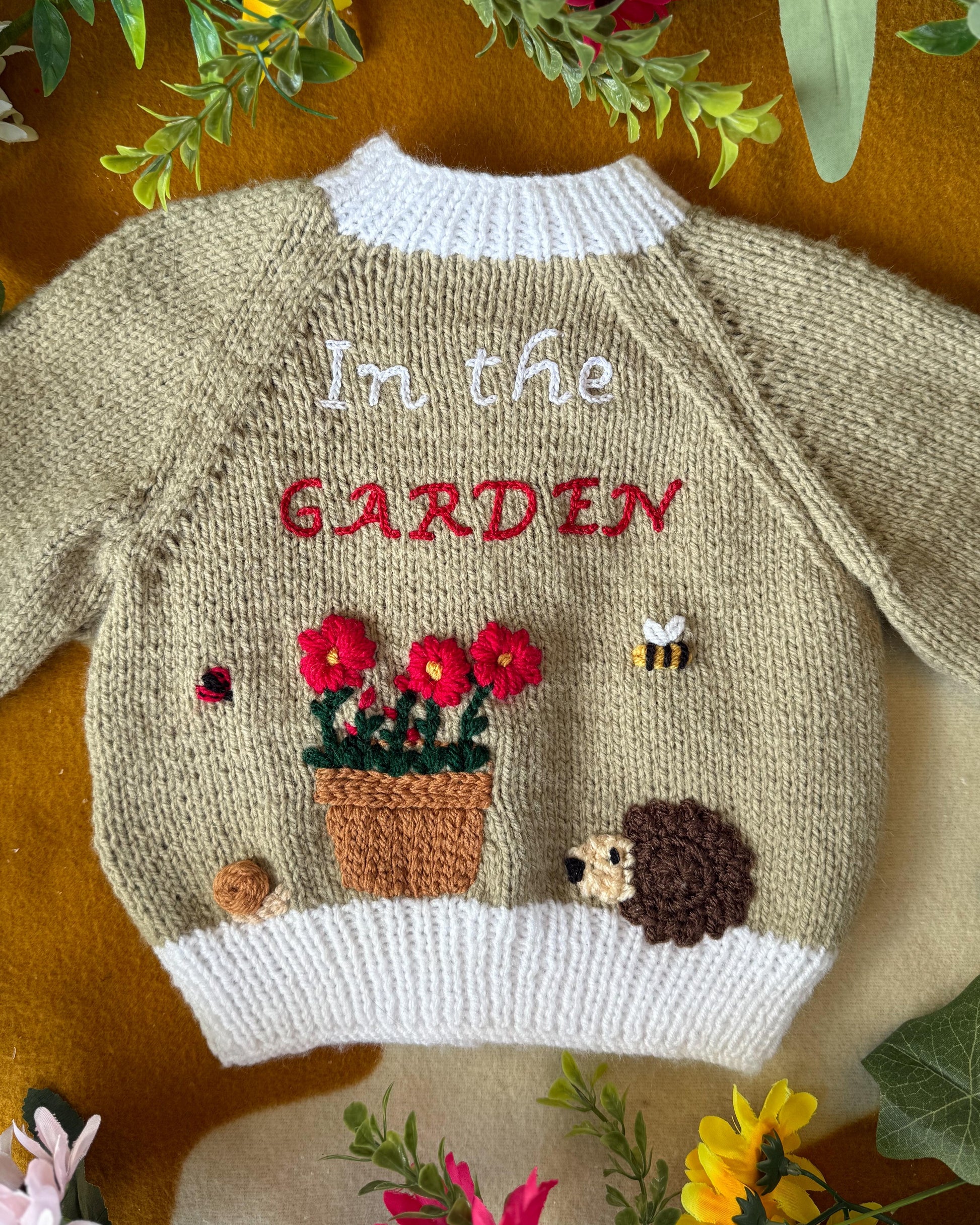 Handmade baby cardigan UK featuring floral garden embroidery and hedgehog detail from Little Flower Knits