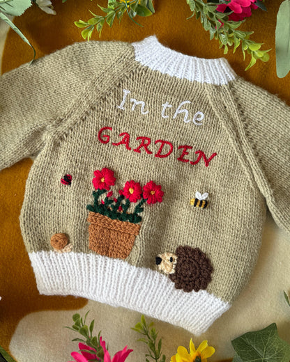 Handmade baby cardigan UK featuring embroidered garden scene with flowers, a hedgehog, and insects