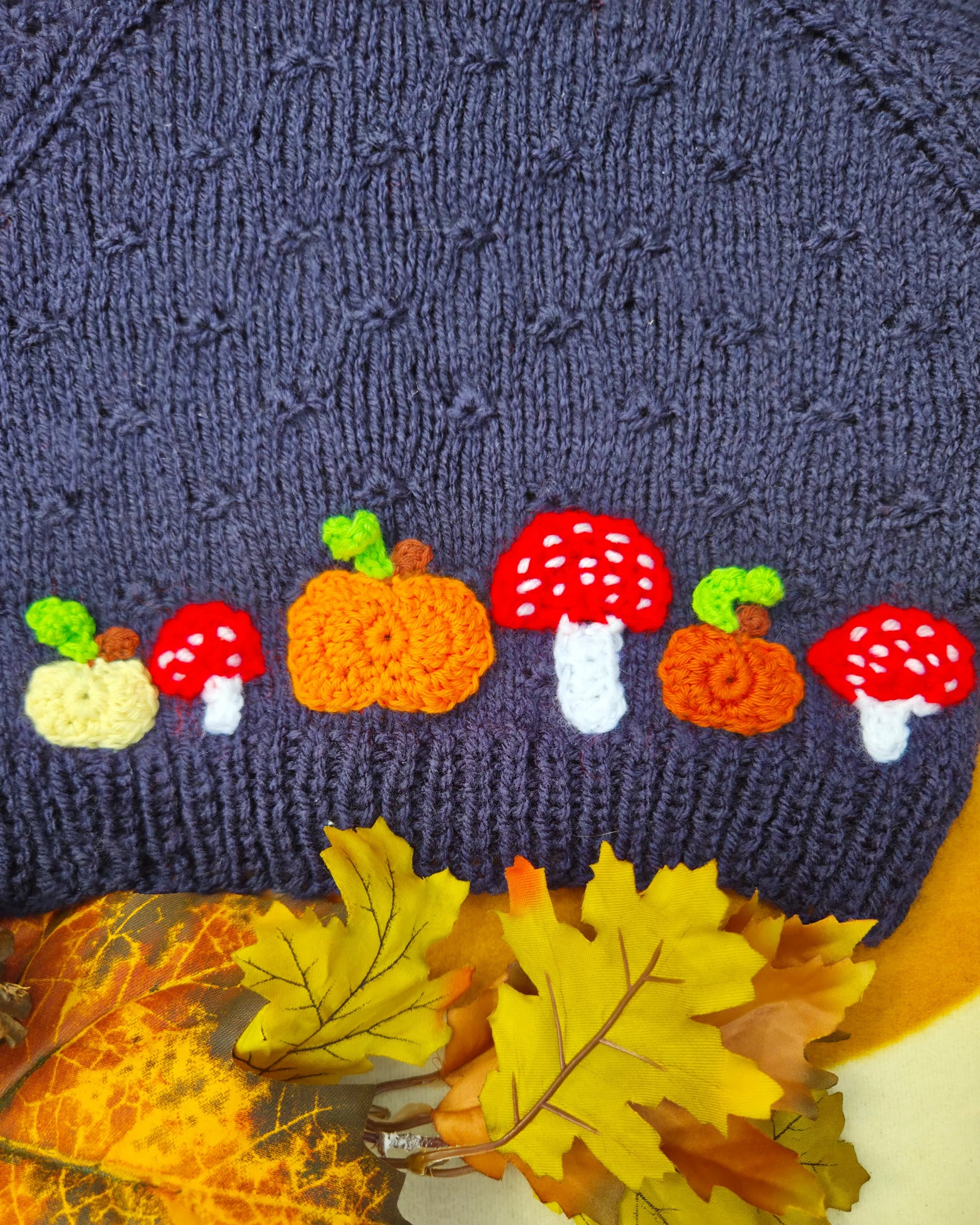 Little Flower Knits dark blue jumper hem with autumn appliques featuring hand-knitted pumpkin and toadstool costume motifs