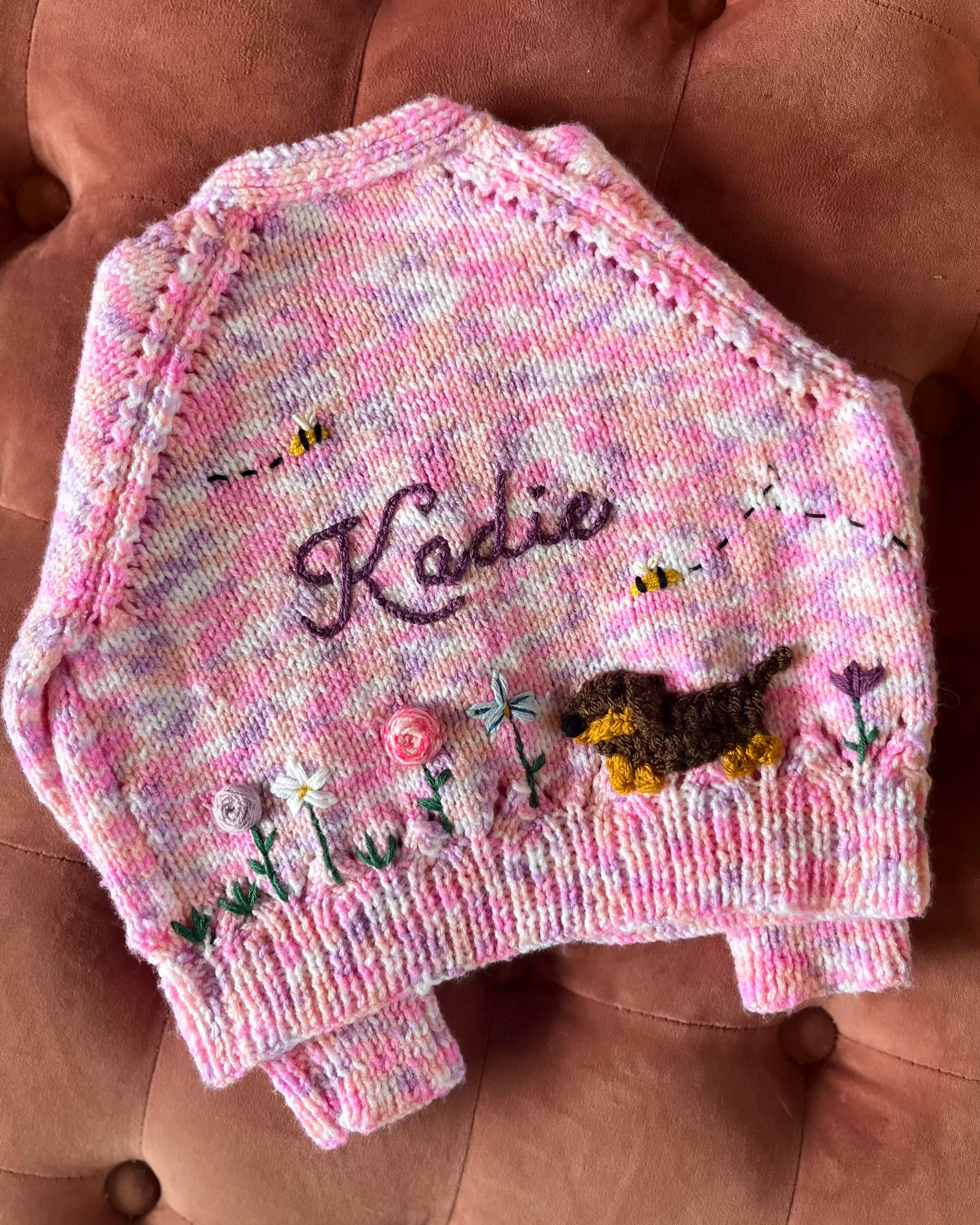 Hand-knitted personalised baby cardigan UK in pink with embroidered flowers, bees, dog and name Kadie