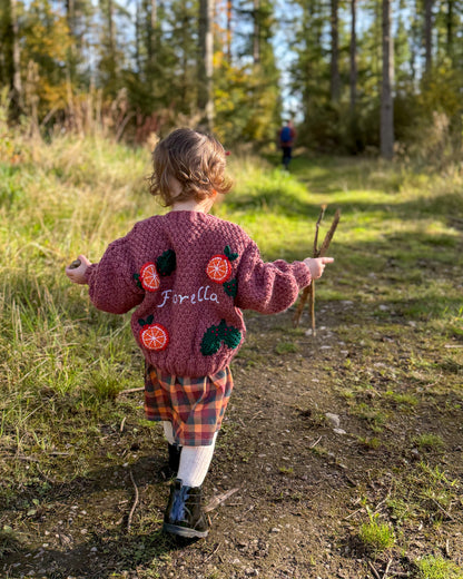 Child wearing a personalised kids cardigan hand knitted with floral embroidery in a forest setting