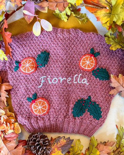 Personalised kids cardigan hand knitted in pink with orange and holly designs, featuring the name Fiorella