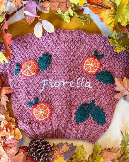 Personalised kids cardigan hand knitted in pink with orange and holly designs, featuring the name Fiorella