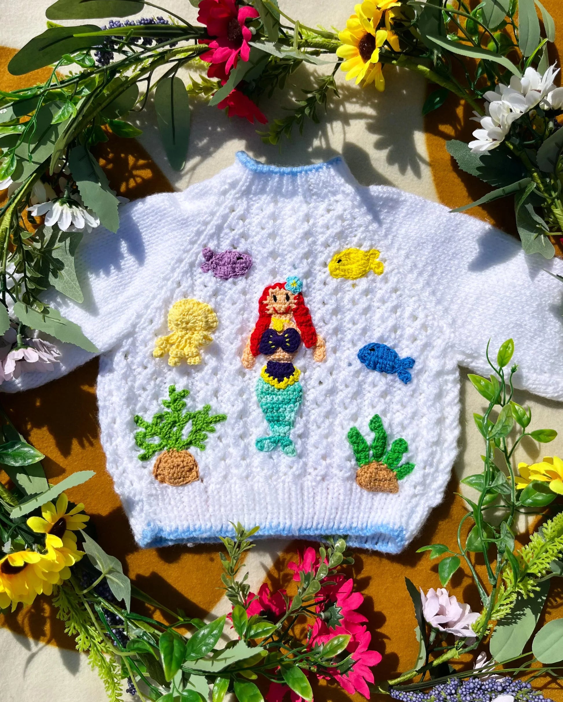 White knitted personalised mermaid cardigan with colourful sea creature designs surrounded by flowers