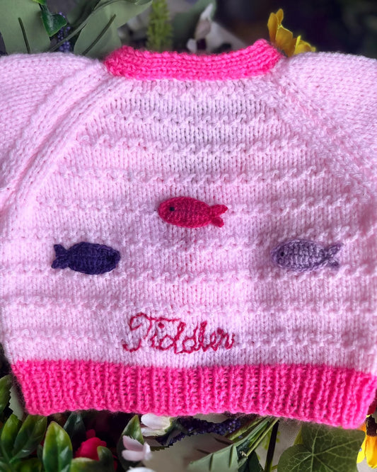 Pink knitted baby cardigan with pink, purple and navy fish buttons and embroidered name by Little Flower Knits unique baby fish cardigan
