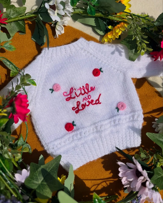 White knitted baby jumper with Little and Loved embroidery surrounded by colourful flowers unique personalised baby gift