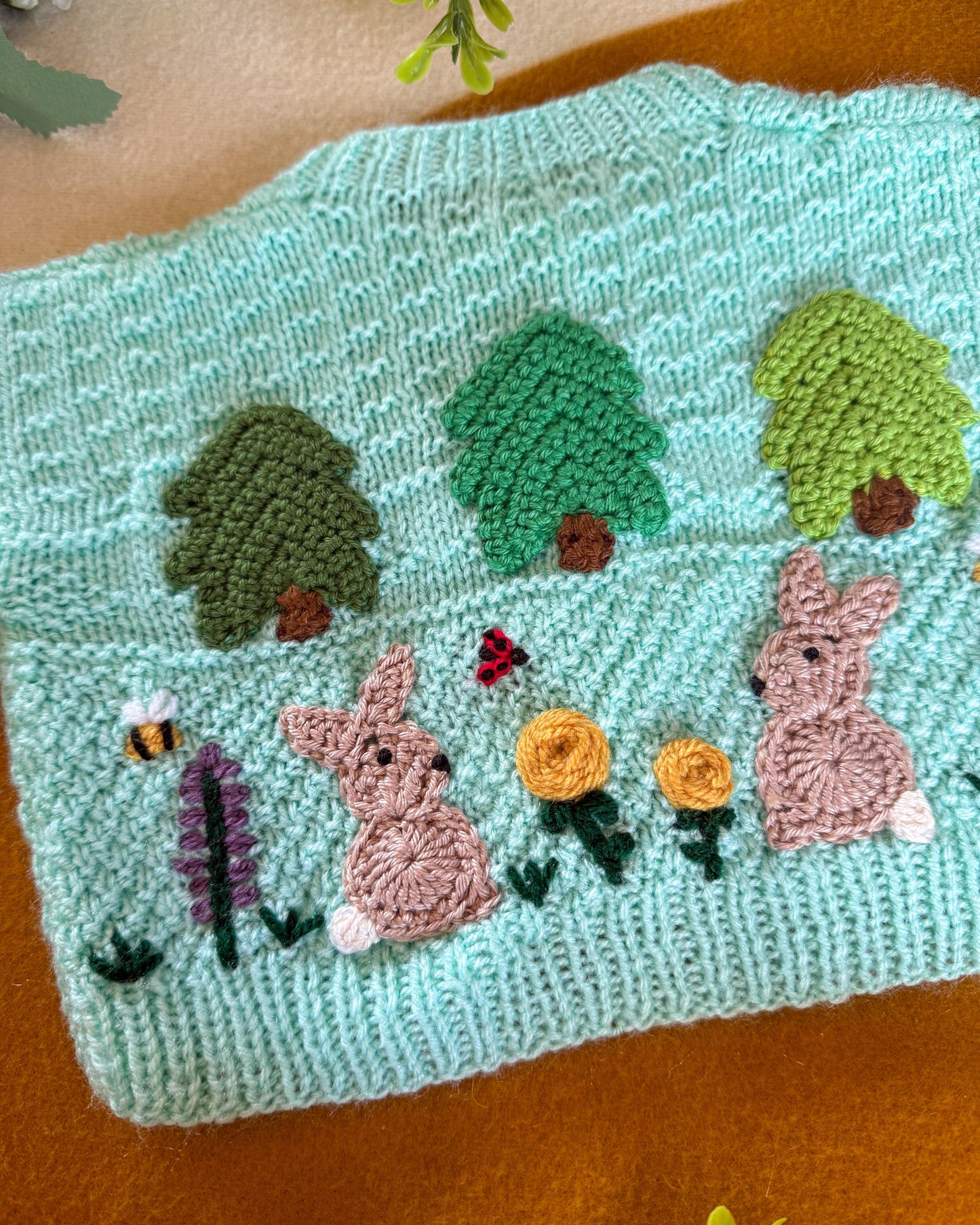 Hand-knitted wildflower meadow baby cardigan featuring cute rabbits and vibrant flowers