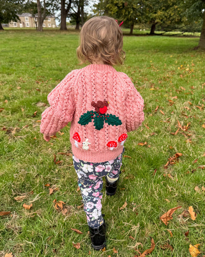 Toddler wearing a pink winter woodland cardigan for toddlers with mushroom and heart designs