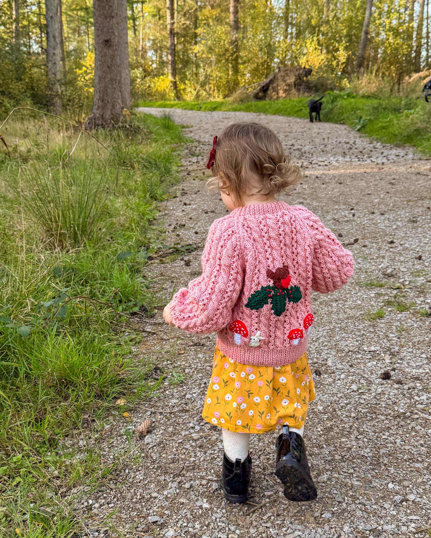 Girl walking on a forest path wearing a pink knitted cardigan with woodland themed kids cardigan design