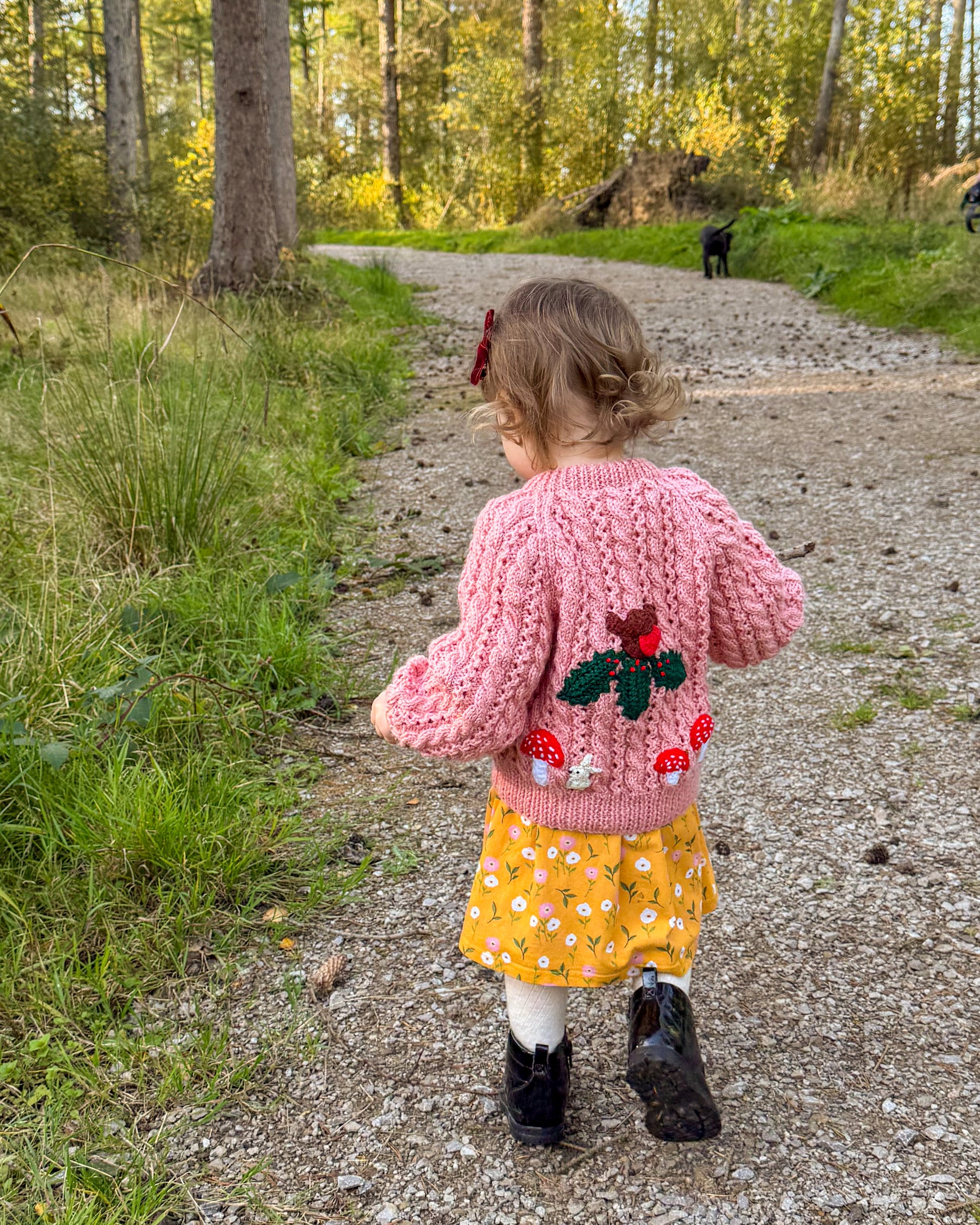 Girl walking on a forest path wearing a pink knitted cardigan with woodland themed kids cardigan design